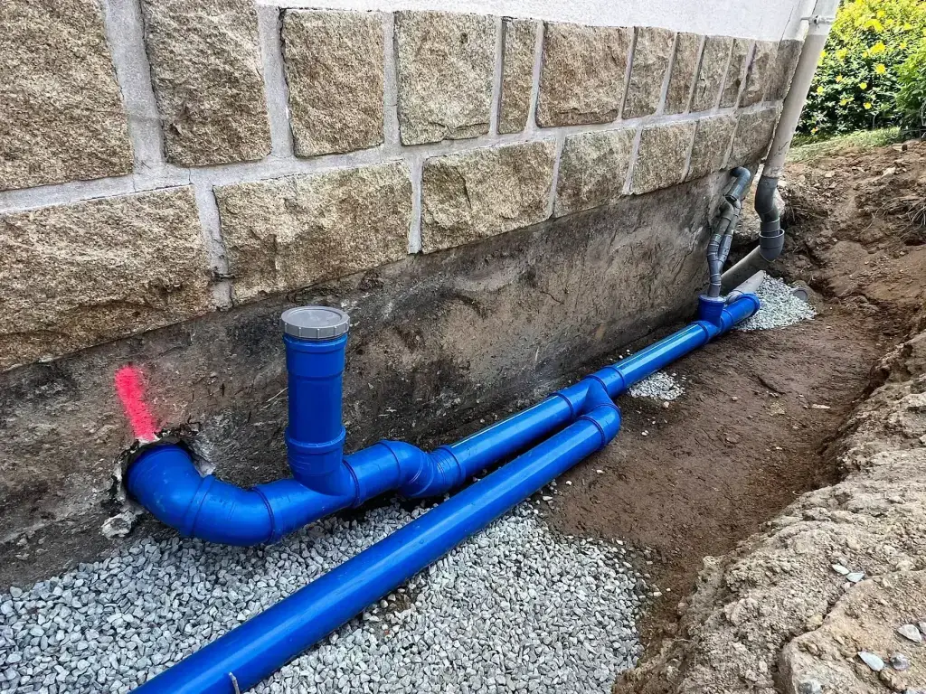 Raccordement des eaux usées en PVC bleu au pied d'une maison en pierre, assainissement en Finistère Sud