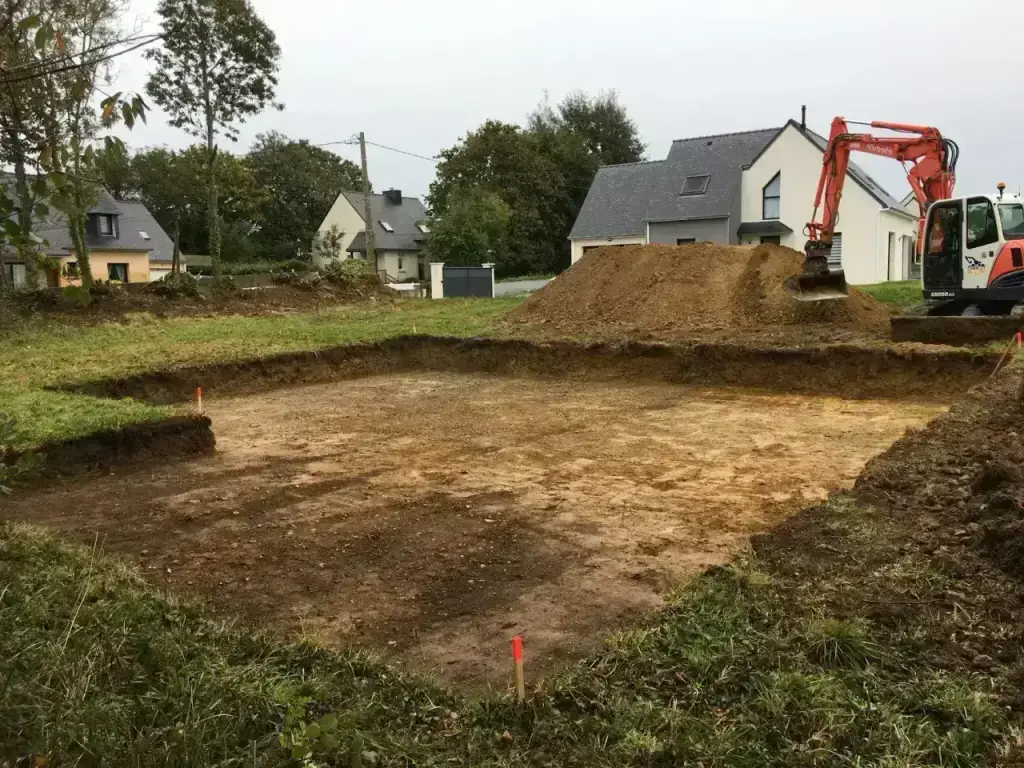 Décaissement de plateforme de maison à la pelle Kubota KX080, maisons du quartier en fond, terrassement en Finistère Sud