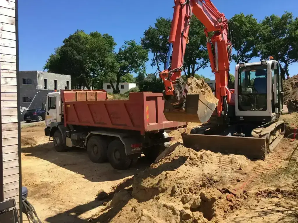 Chargement de terre dans un camion-benne 6x4 à la pelle Kubota en plein soleil, terrassement en Finistère Sud