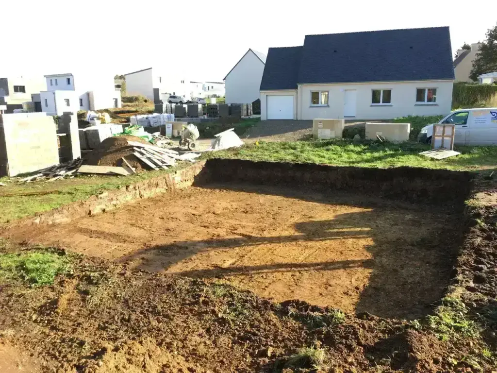 Plateforme de maison décaissée en lotissement devant une construction neuve, soleil rasant, terrassement en Finistère Sud
