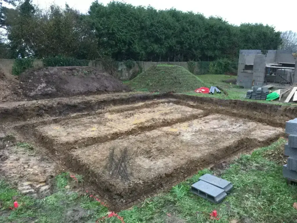 Fouilles de fondations avec armatures en attente et parpaings le long d'une haie de cyprès, terrassement en Finistère Sud